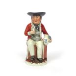 A Sailor Toby jug c.1800-10, seated on his sea chest and holding a glass in his right hand, a blue