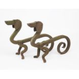 A pair of patinated iron fire dogs probably designed by Edouard Schenck, each modelled as a stylised