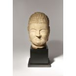 A CHINESE CARVED LIMESTONE HEAD OF BUDDHA NORTHERN QI DYNASTY His serene face with downcast eyes set