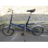 A vintage Moulton Deluxe bicycle with navy blue colourway, long folding kick stand and two unused