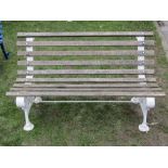 A two seat garden bench with weathered timber lathes, raised on a pair of decorative Victorian