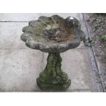 A weathered cast composition stone bird bath of shell shaped form, raised on a pedestal with