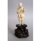 Carved ivory figure of a standing fisherman upon a carved wooden plinth base, 15cm high total