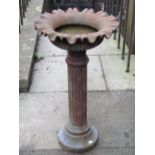 A weathered cast iron bird bath/planter, the squat circular bowl with crimped edge raised on a