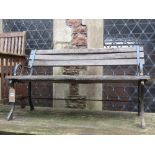 A two seat garden bench with weathered timber lathes, raised on decorative cast iron end supports,
