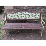 A two seat garden bench with weathered timber lathes raised on a pair of decorative pierced cast