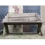 A weathered West African iroko wood two seat garden bench with shaped ends and pegged frame and