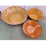 Three dairy bowls in terracotta with freestyle slip decoration, the largest 63cm diameter, the