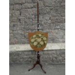 A simple 19th century oak pole screen supporting a shield shaped panel with hand worked floral