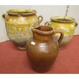 Two graduated terracotta vessels with loop handles with ochre coloured glazing, together with a