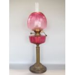 A late 19th century cast brass Corinthian column oil lamp, with cranberry glass reservoir and fluted