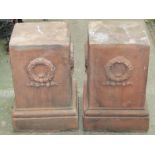 A pair of contemporary reproduction composition stone urn pedestals of square cut and stepped form