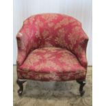 A low Edwardian tub chair with shaped outline, upholstered finish and short cabriole forelegs