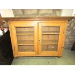 A stripped pine kitchen wall cabinet enclosed by a pair of rectangular glazed panelled doors