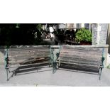 A pair of two seat garden benches with stained timber lathes and decorative green painted cast