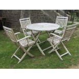 A weathered teak folding garden table, the circular quarter slatted top raised on x framed supports,