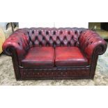 A pair of small two seat Chesterfield sofas in a Victorian style, upholstered in a maroon coloured
