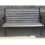 A two seat garden bench with weathered timber lathes and decorative pierced cast iron ends with