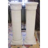 A pair of buff coloured pedestals with classical cylindrical fluted columns and caps with foliate