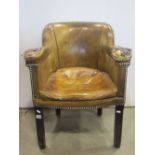 An antique Georgian style tub chair with shaped outline and worn mustard coloured leather upholstery