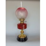 Late 19th century cast brass oil lamp with faceted cranberry glass reservoir, upon a turned column