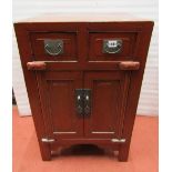 A small floor standing Chinese crimson lacquered side cupboard enclosed by two drawers and two