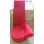 A low retro style upholstered chair with tall tapered back and single roll arm and circular seat