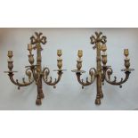 A pair of gilt cast metal twin branch wall lights with scroll cornucopia branches and ribbon back