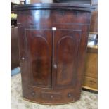 A 19th century mahogany bow fronted hanging corner cupboard enclosed by a pair of arched panelled