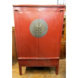 A Chinese red lacquered cabinet enclosed by two doors over two frieze drawers, with central brass