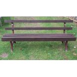 A vintage railway platform type bench with stained wooden slats, raised on a pair of painted cast