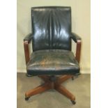 A vintage swivel office desk chair, with green leather upholstered seat, back and arms, raised on