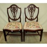 A pair of Georgian mahogany dining chairs in the Hepplewhite style with shield shaped backs,