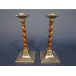 Pair of arts and crafts silver and barley twist oak candlesticks, the silver with planished