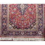 Traditional Persian rug with central blue medallion framed by scrolled foliage upon a red ground,