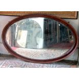 A large Edwardian oak wall mirror of oval form with moulded frame enclosing a bevelled edge plate,
