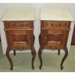 A pair of oak bedside cupboards of square cut form with white marble tops, each enclosed by a single