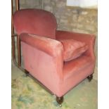 An Edwardian easy chair with shaped outline, rolled arms and pink coloured upholstery, loose seat