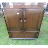 An Ercol stained elm side cupboard enclosed by a pair of rectangular doors over a hinged fall