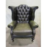 A green leather buttoned upholstered winged armchair in the Georgian style with shaped outline,