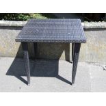 A contemporary coated wicker effect garden terrace table, the square top raised on four tapered