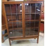 A teak bookcase/side cabinet freestanding and enclosed by a pair of rectangular leaded light