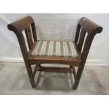 An arts and crafts oak stool with raised and rolled arms, pierced splats, upholstered pad seat and