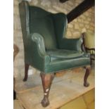 A wing armchair in the Georgian style with shaped outline, faux green leather upholstery and loose