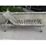 A weathered teak garden lounger with slatted seat and adjustable headrest