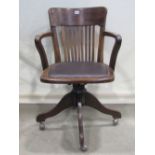 An Edwardian/1920s swivel office desk chair, the stained beechwood frame with upholstered pad seat