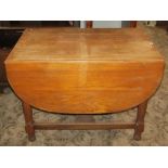 A medium to light oak drop leaf dining table, raised on four turned legs united by a central