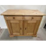 A stripped pine side cupboard enclosed by a pair of rectangular panelled doors beneath two frieze