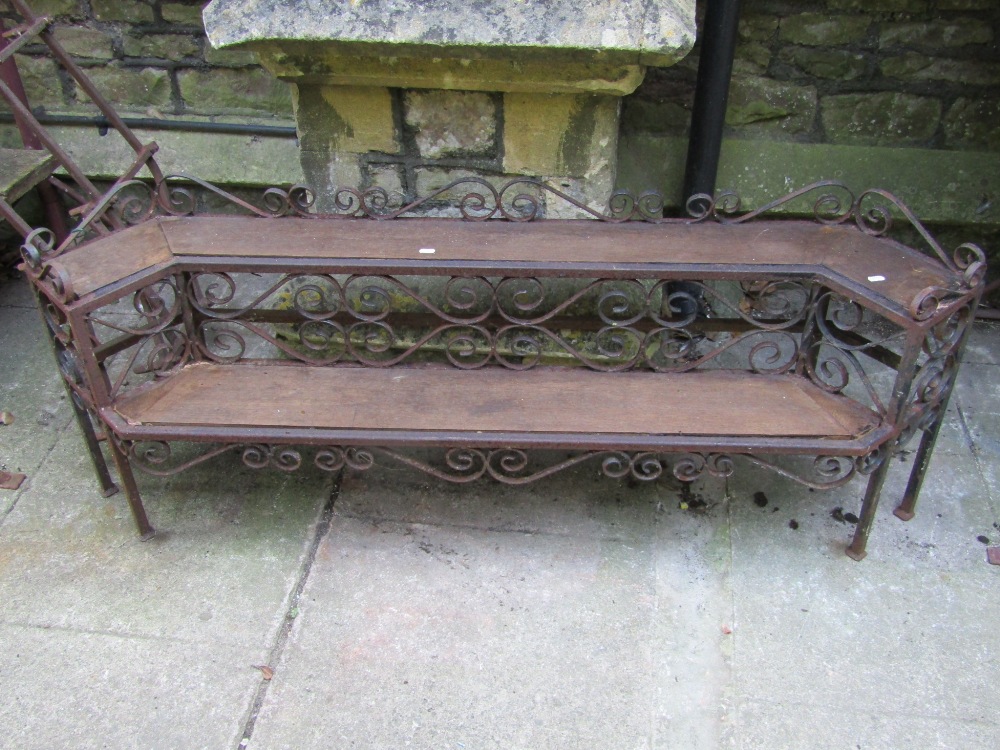 A low two tier plant stand of stepped form, the iron frame with decorative scroll work detail and