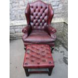 A reproduction Georgian style brown leather upholstered wing armchair with shaped outline, button